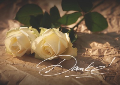 Grusskarte mit einem Foto von weißen Rosen und handgeschriebenen Danke! in weiß.