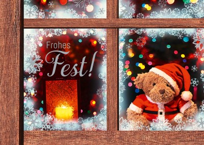 Teddy im verschneiten Fenster mit Weihnachtsmütze wünscht frohes